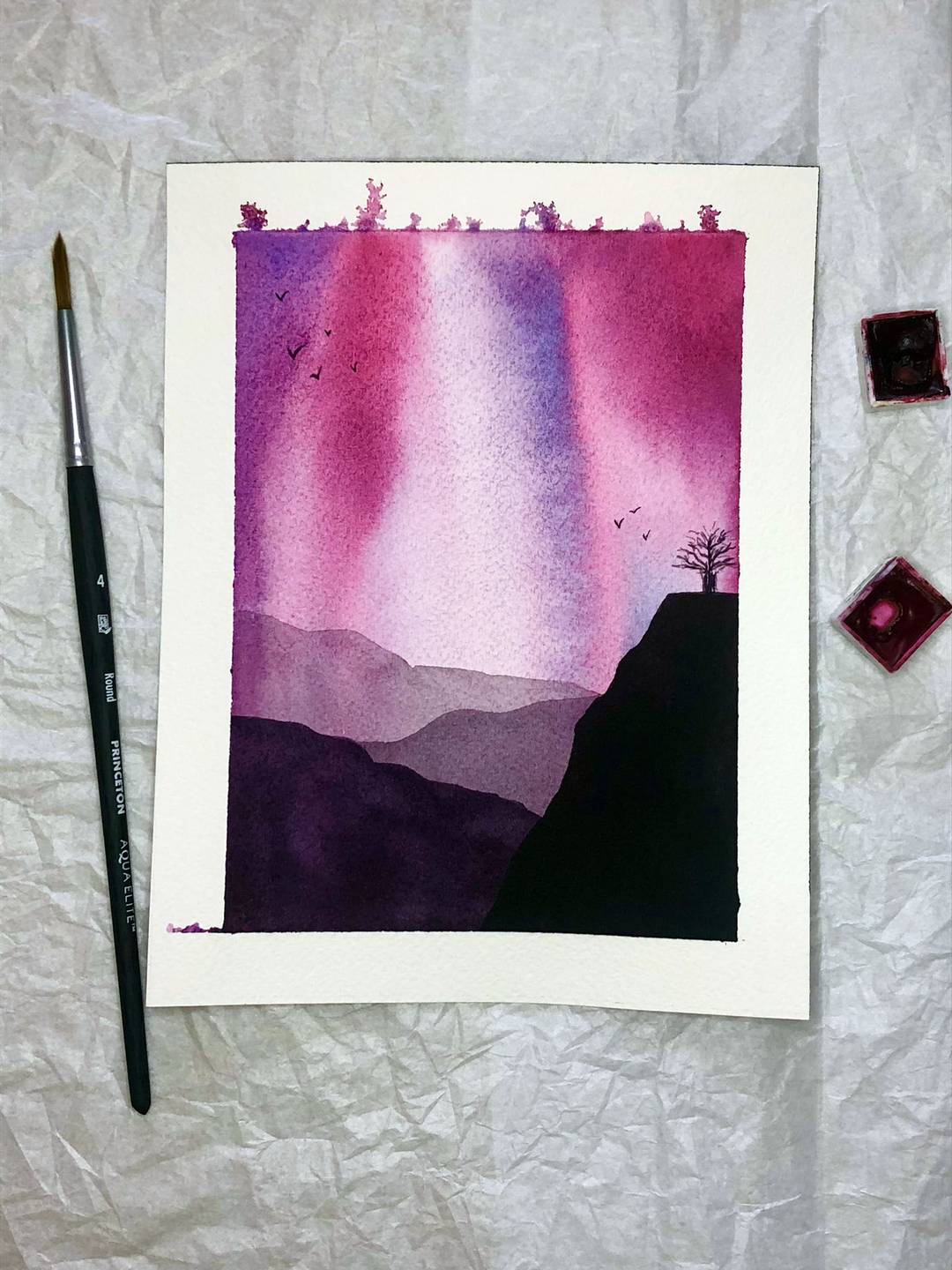watercolor painting of silhouetted hills against a purple and pink sky with a tree and small birdss