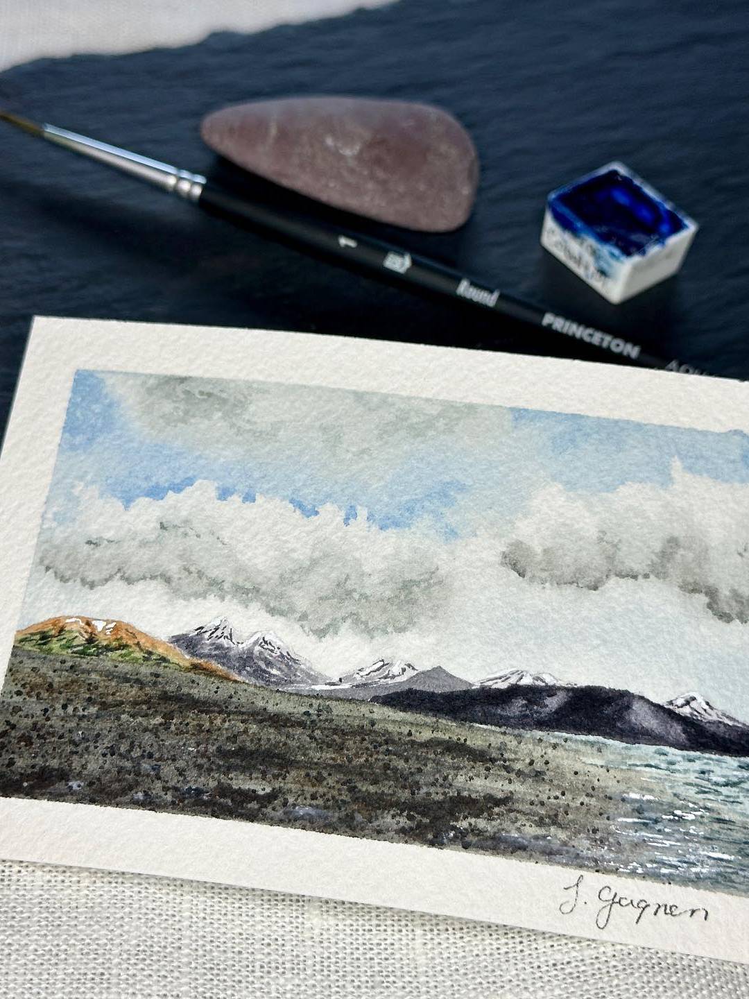 close up of a watercolor landscape painting with mountains behind a beach