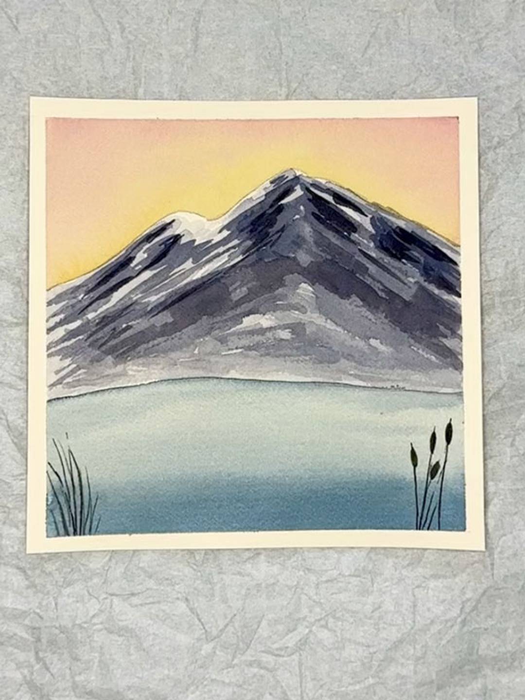 watercolor painting of a snow capped mountain with a sunset sky and a lake in the foreground