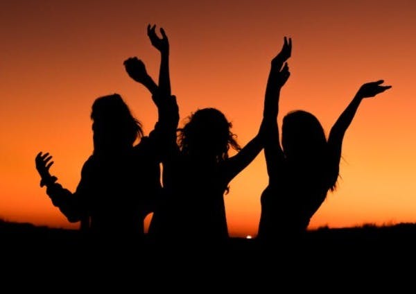 silhouette of three woman with hands on the air while dancing during sunset