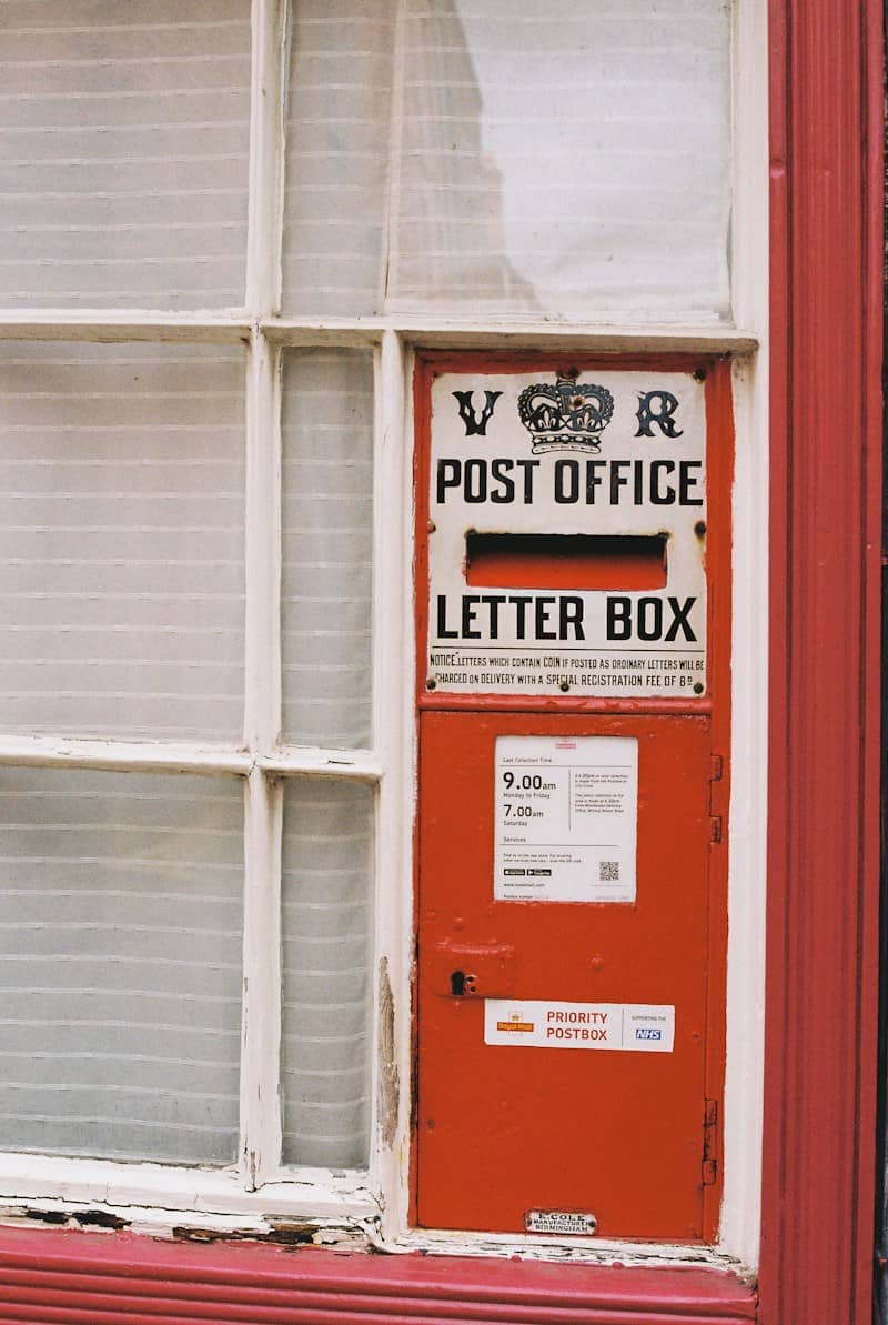 A vintage red wall-mounted post office letter box with a crown emblem