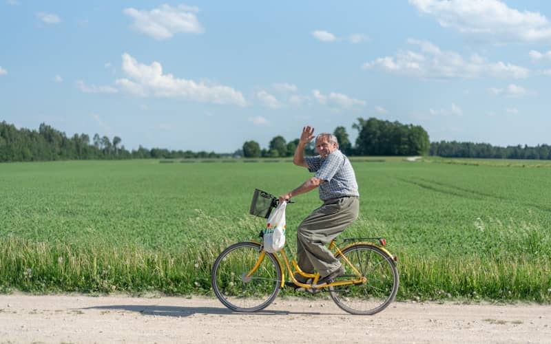 Older man on yellow bicycle waves on a country road.