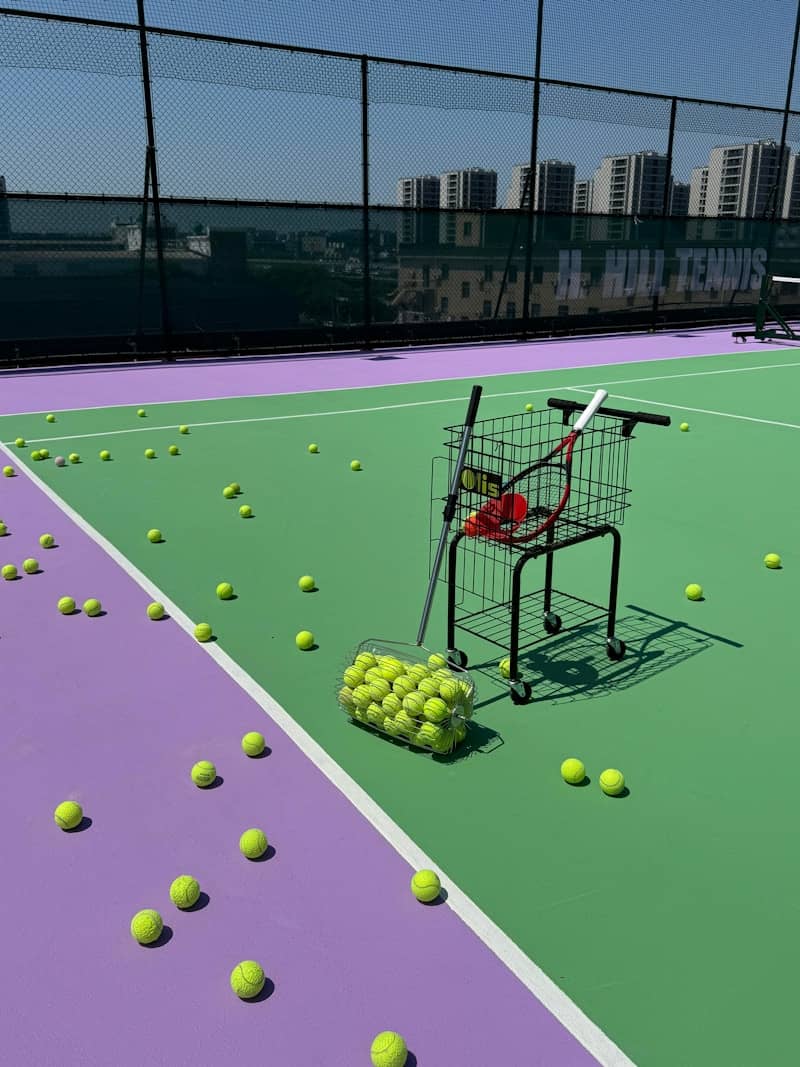 Tennis court with scattered balls, rackets, and a ball cart.