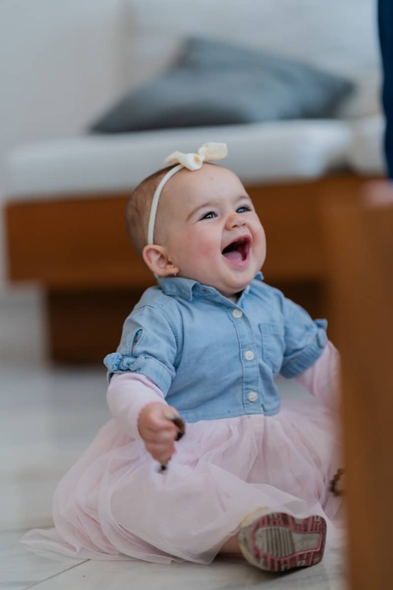 A laughing baby wearing a denim shirt and pink tulle skirt with a headband