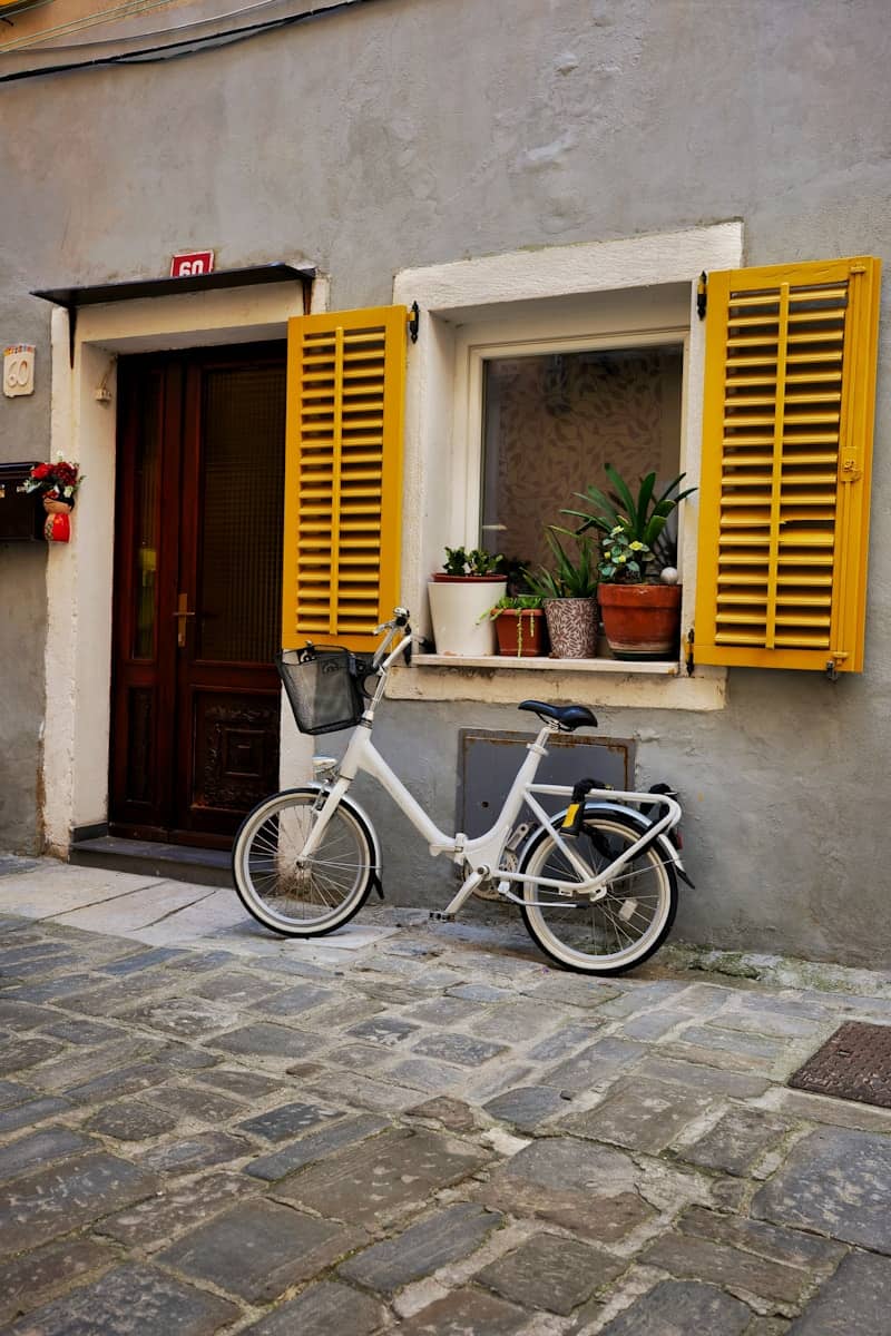 White bicycle parked outside a building with yellow window shutters.