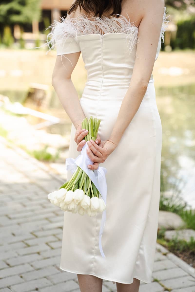 Woman in white dress holding white tulips behind back.