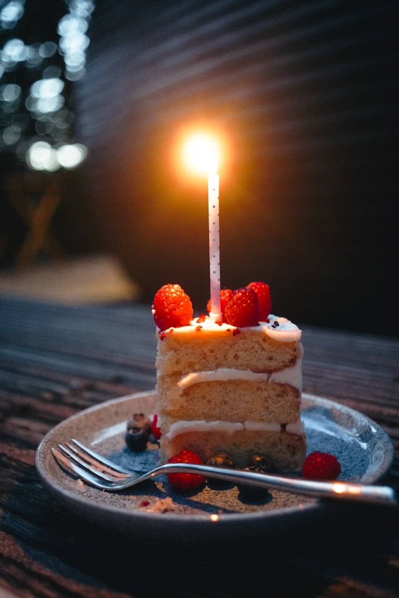 A slice of cake with a lit candle and raspberries.