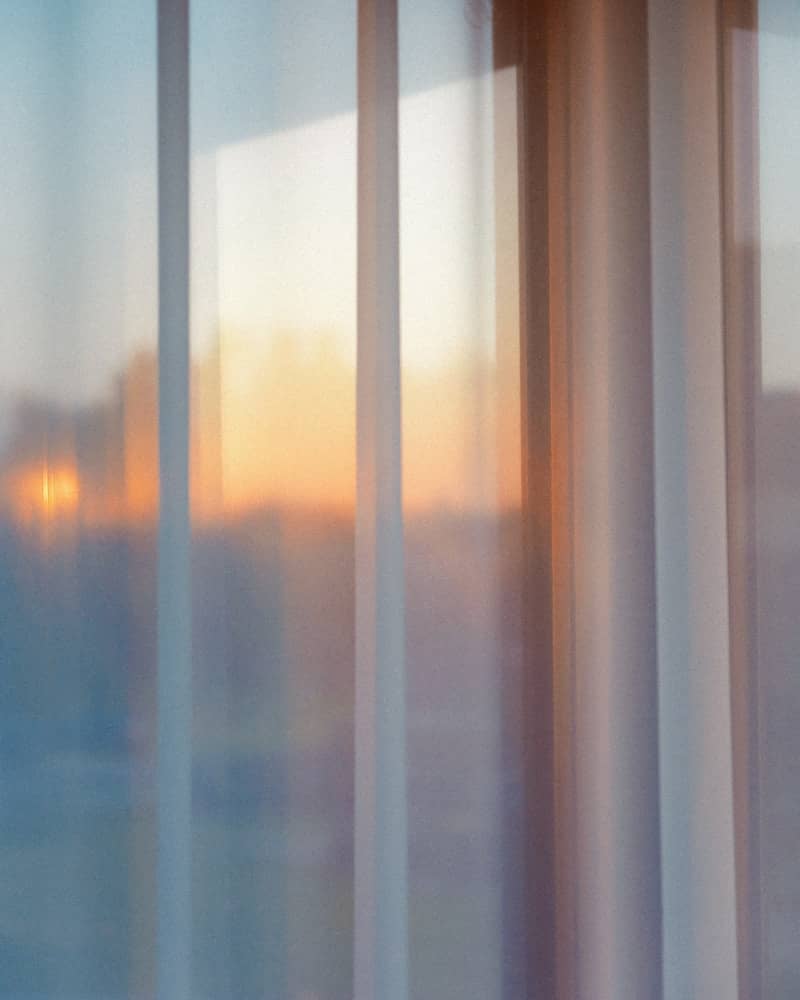 Sunset light filters through sheer curtains on a window.