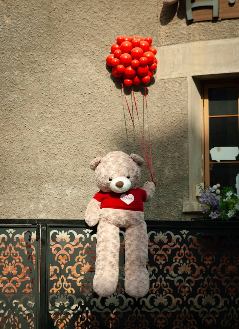 A teddy bear holding a bunch of red balloons