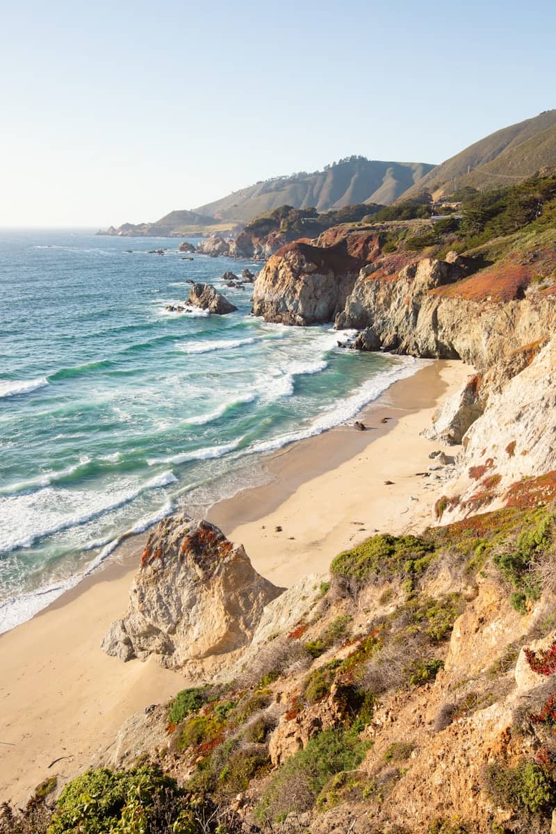 Scenic coastline with sandy beach, ocean waves, and rugged cliffs.