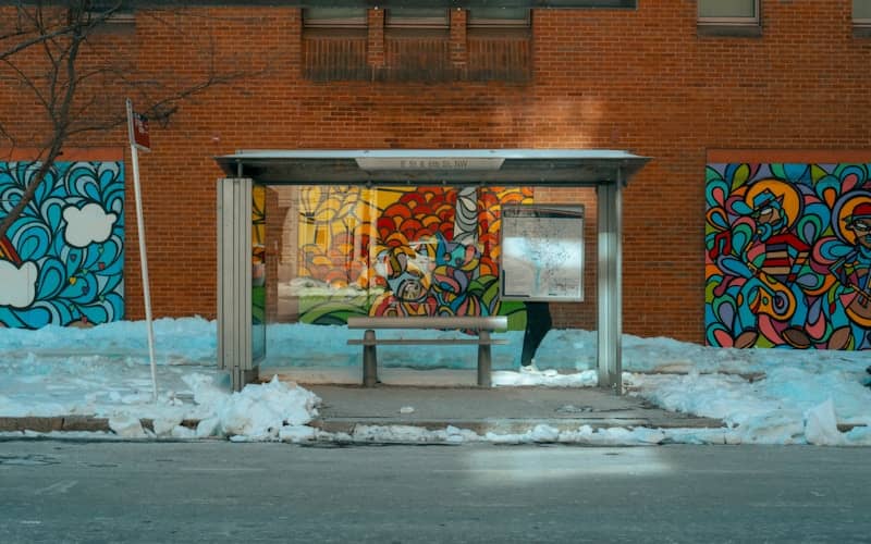 A bus stop shelter with colorful murals and snow.
