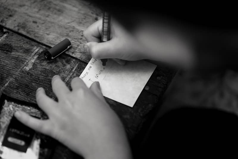 A person writing on a small card with a pen on a wooden table