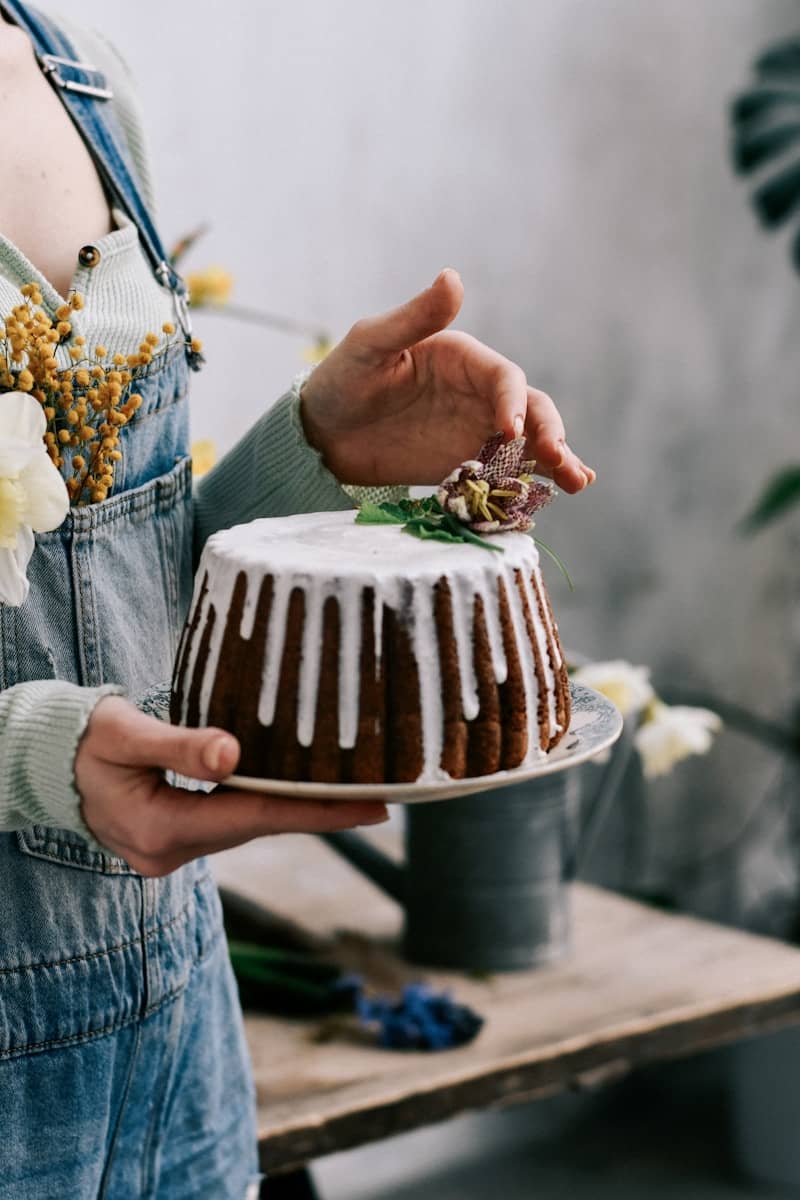 Person holding a bundt cake with white icing and flowers