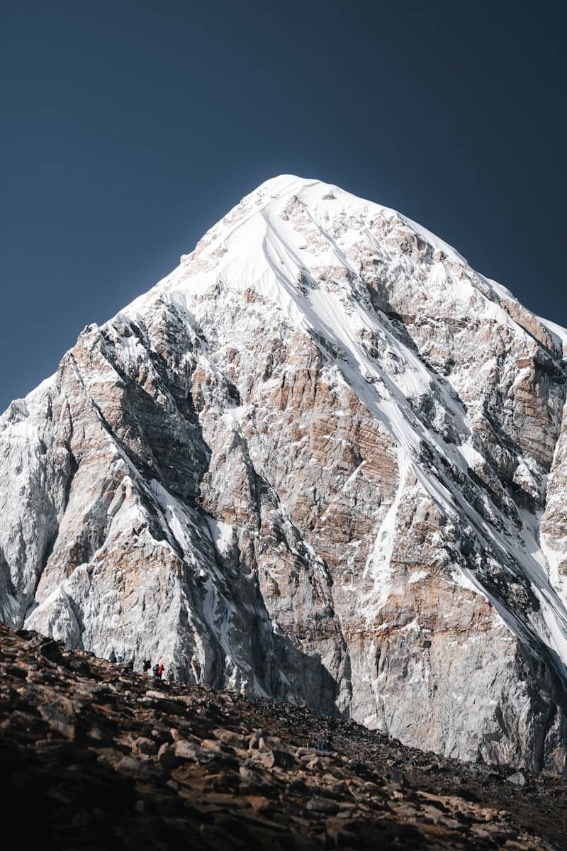 Snow-covered mountain peak with hikers on rocky slope.