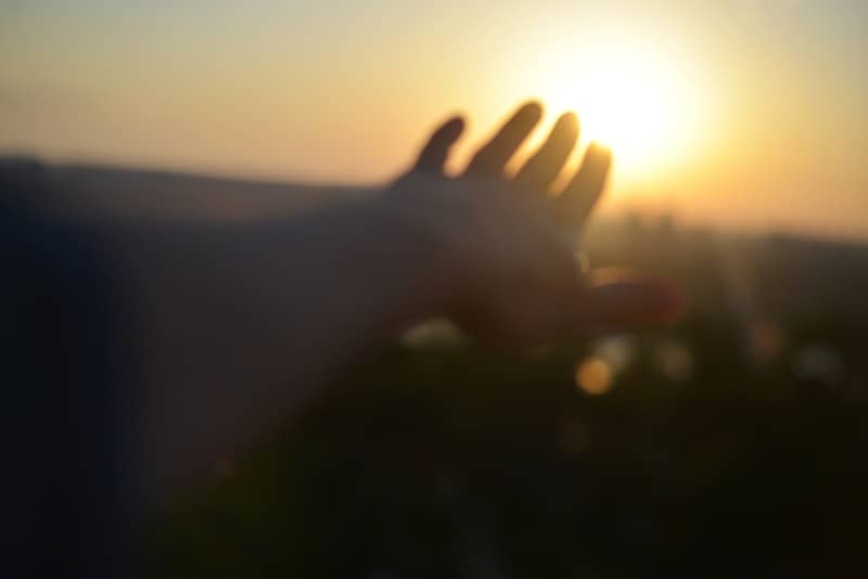 A blurred hand reaches towards the bright setting sun.