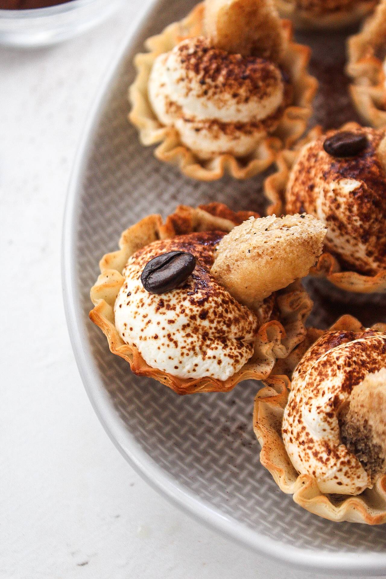 a close up of a tiramisu phyllo cup filled with mascarpone topped with an espresso bean and a soaked lady finger