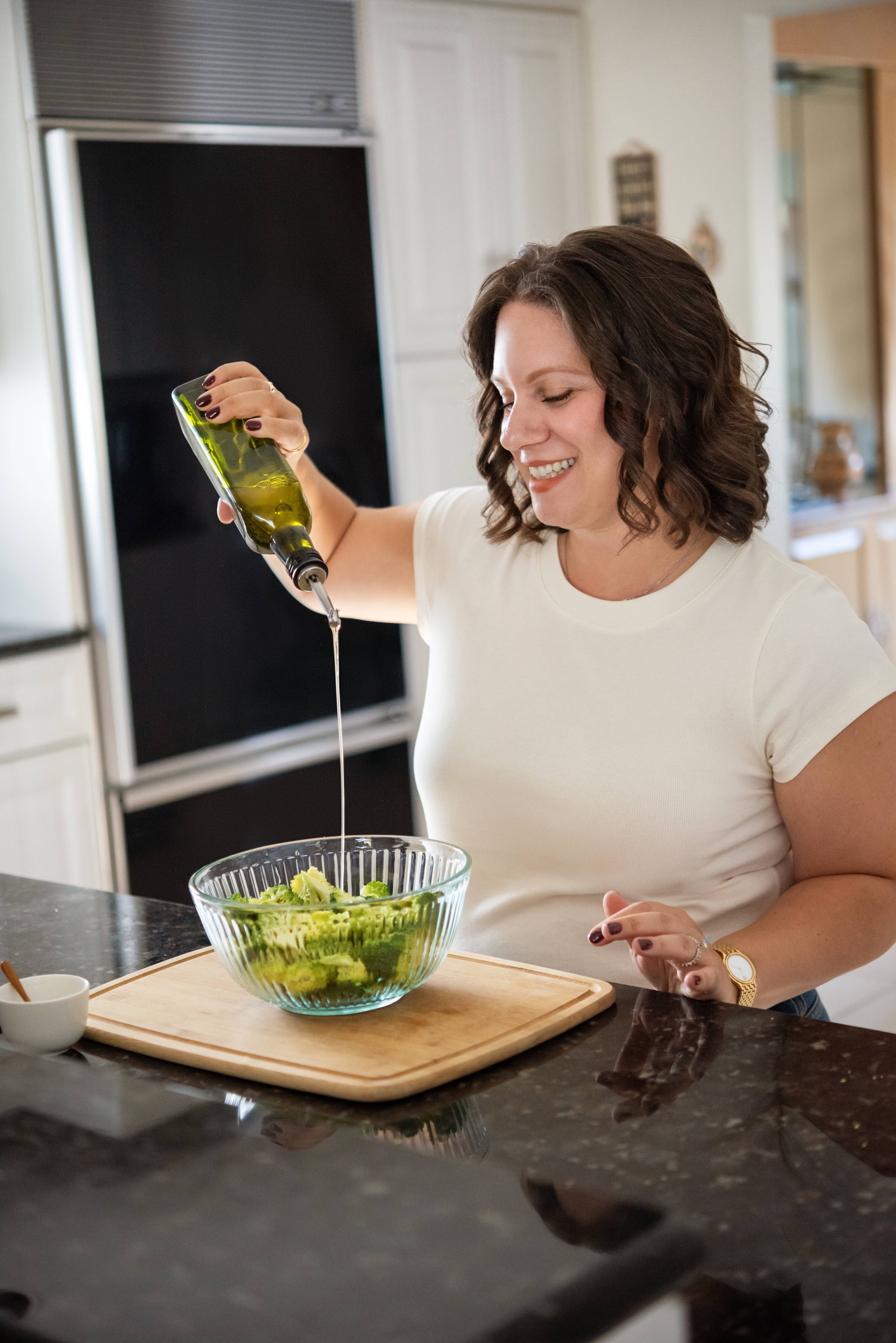 a photo of morgan pouring oil into a bowl of broccoli.