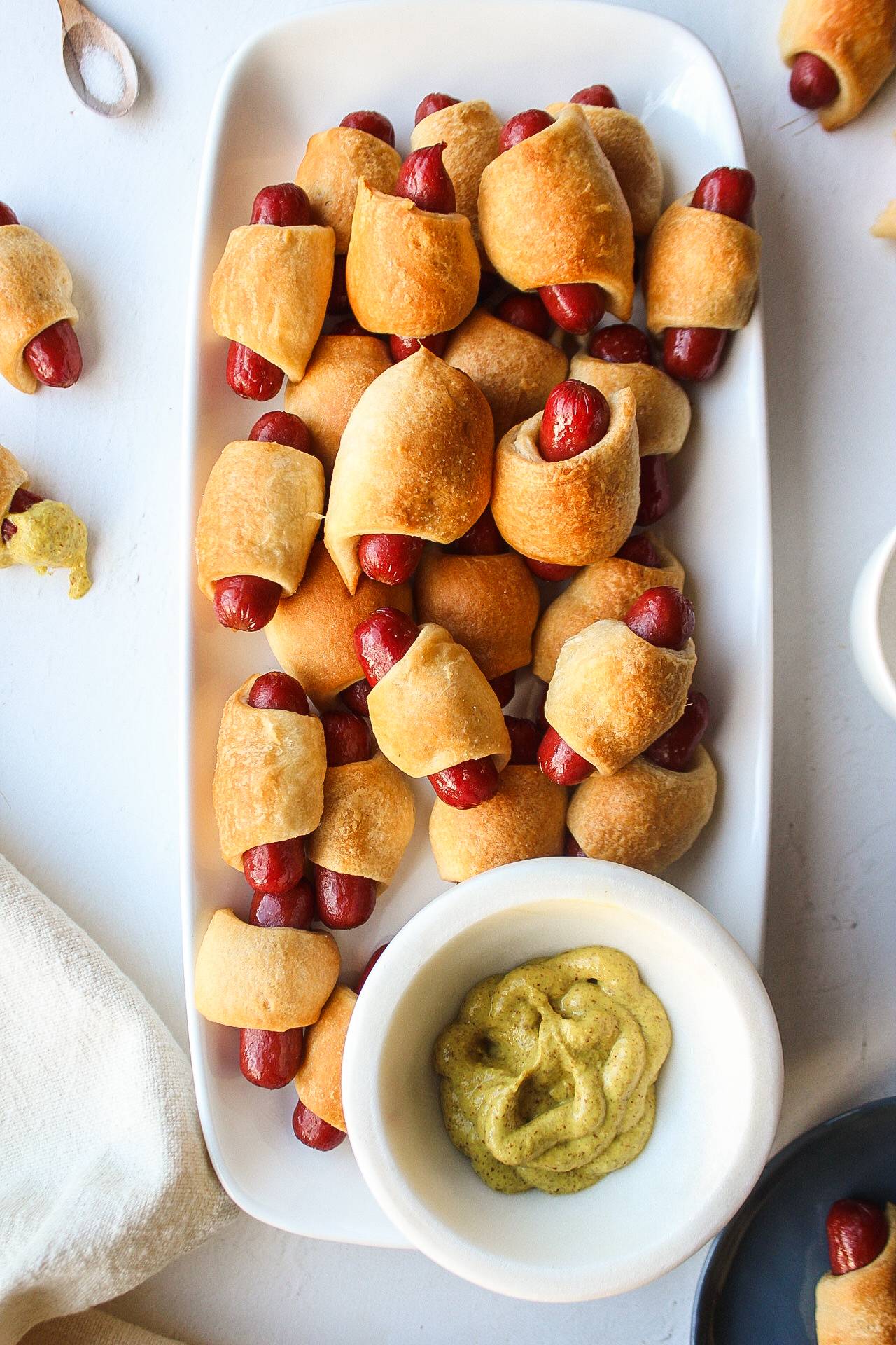 a platter of homemade crescent roll hot dogs with mustard on the side.