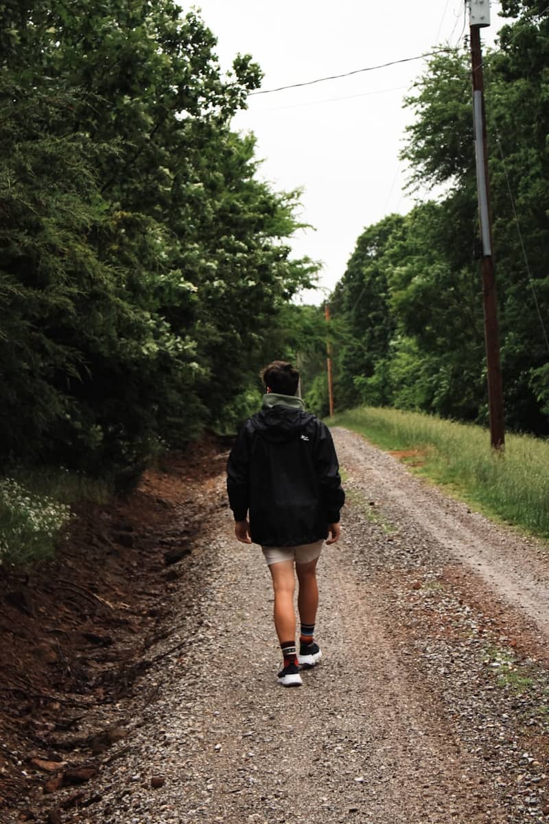 Man walking down a gravel road through trees