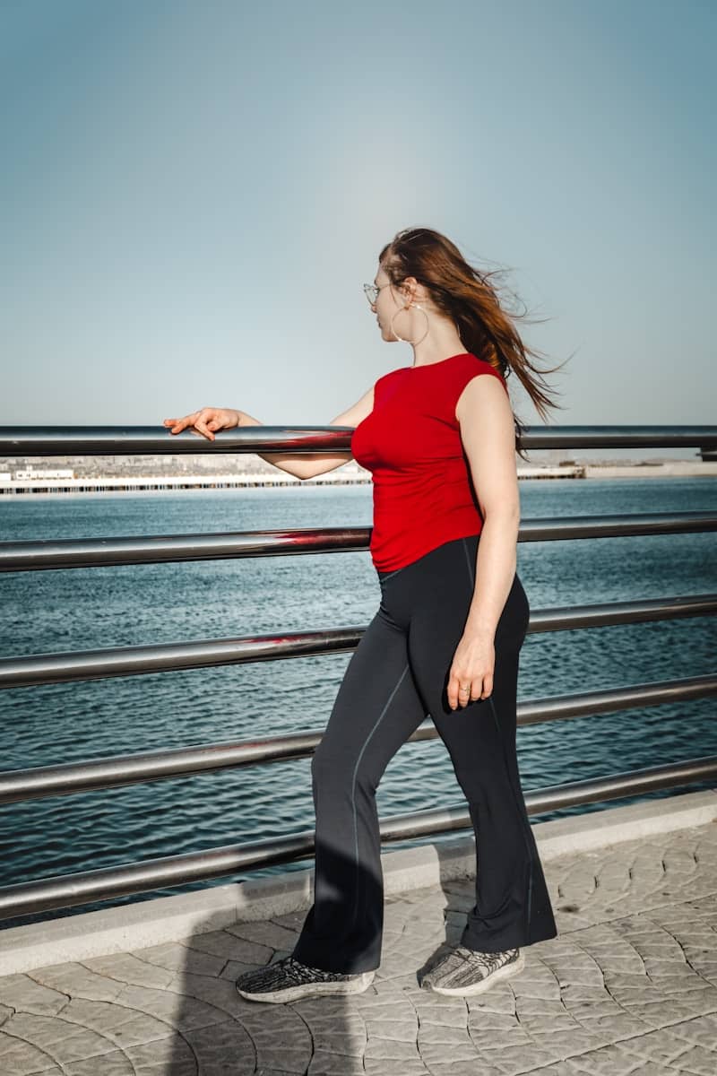 Woman in red top and black pants by the water.