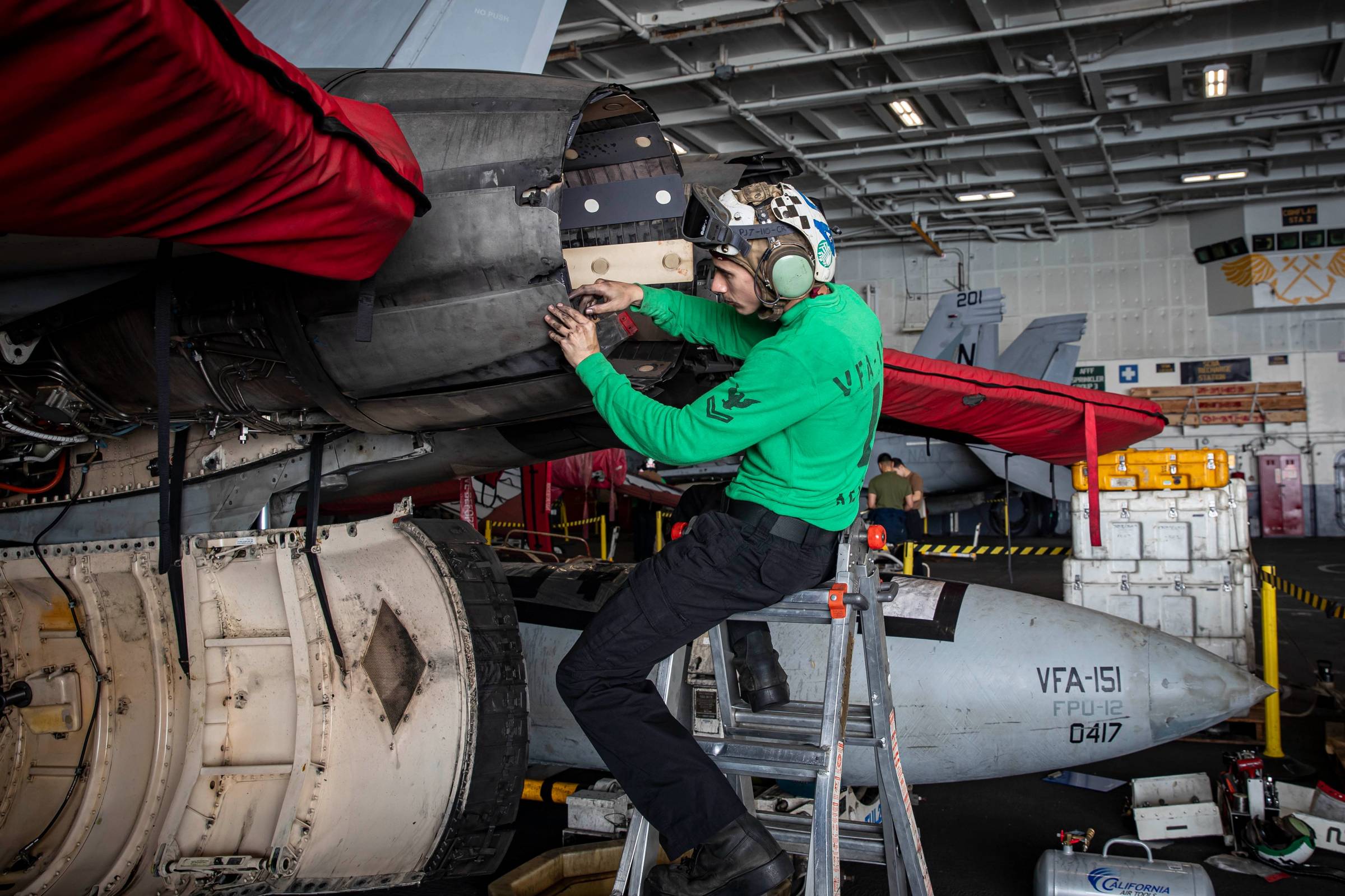 A sailor assigned to VFA-151 performs maintenance on an F/A-18 in the hangar bay of USS Abraham Lincoln (CVN 72) as the carrier transits the Indian Ocean en route to the Middle East, Jan. 26, 2026. (CENTCOM via X)