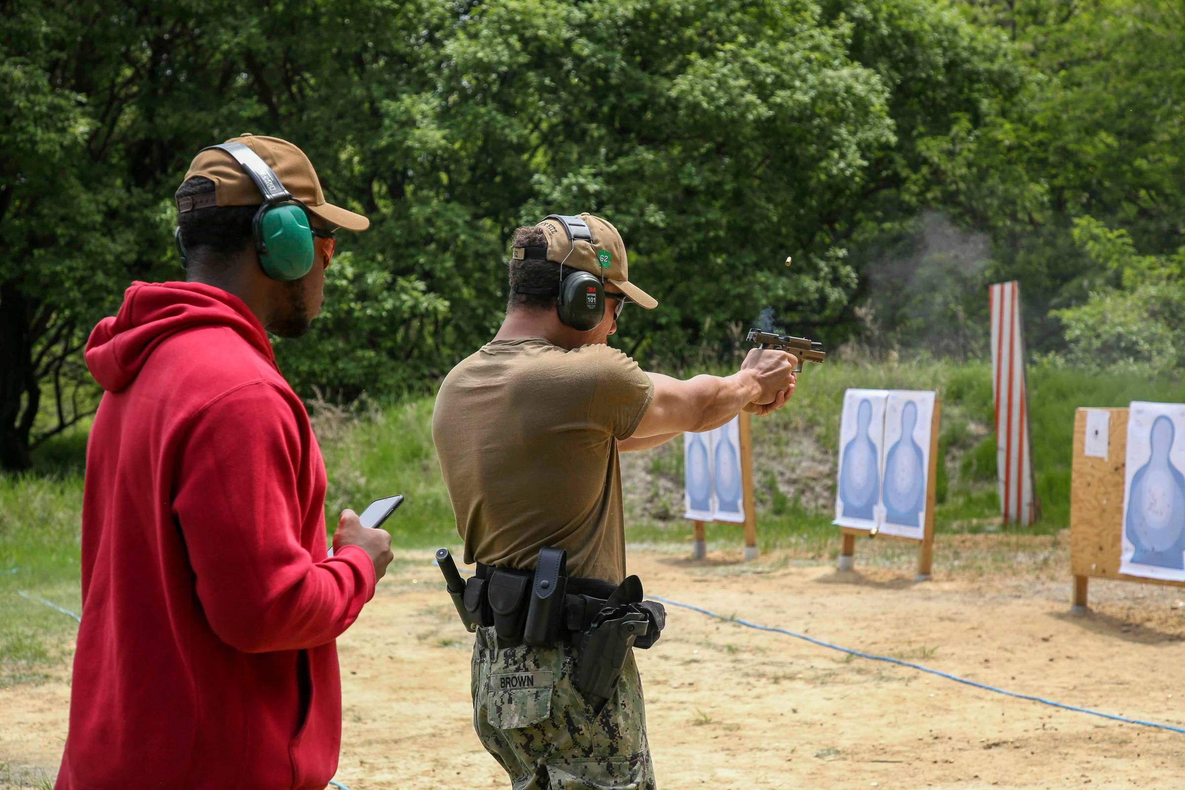 A Master-at-Arms observes a Gunner’s Mate firing an M18 during a weapons qualification, May 10, 2022. (U.S. Navy photo by Master-at-Arms 2nd Class Le McNeill)