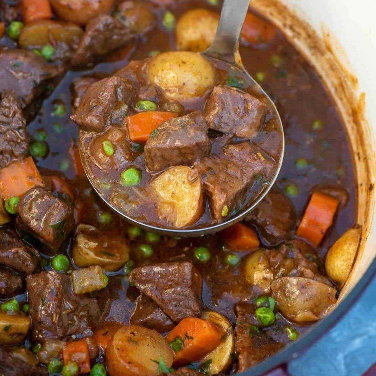 A ladle scooping beef stew from a Dutch oven.