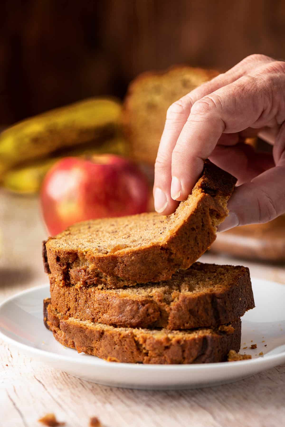 A hand pulling away a slice of apple banana bread from a stack.