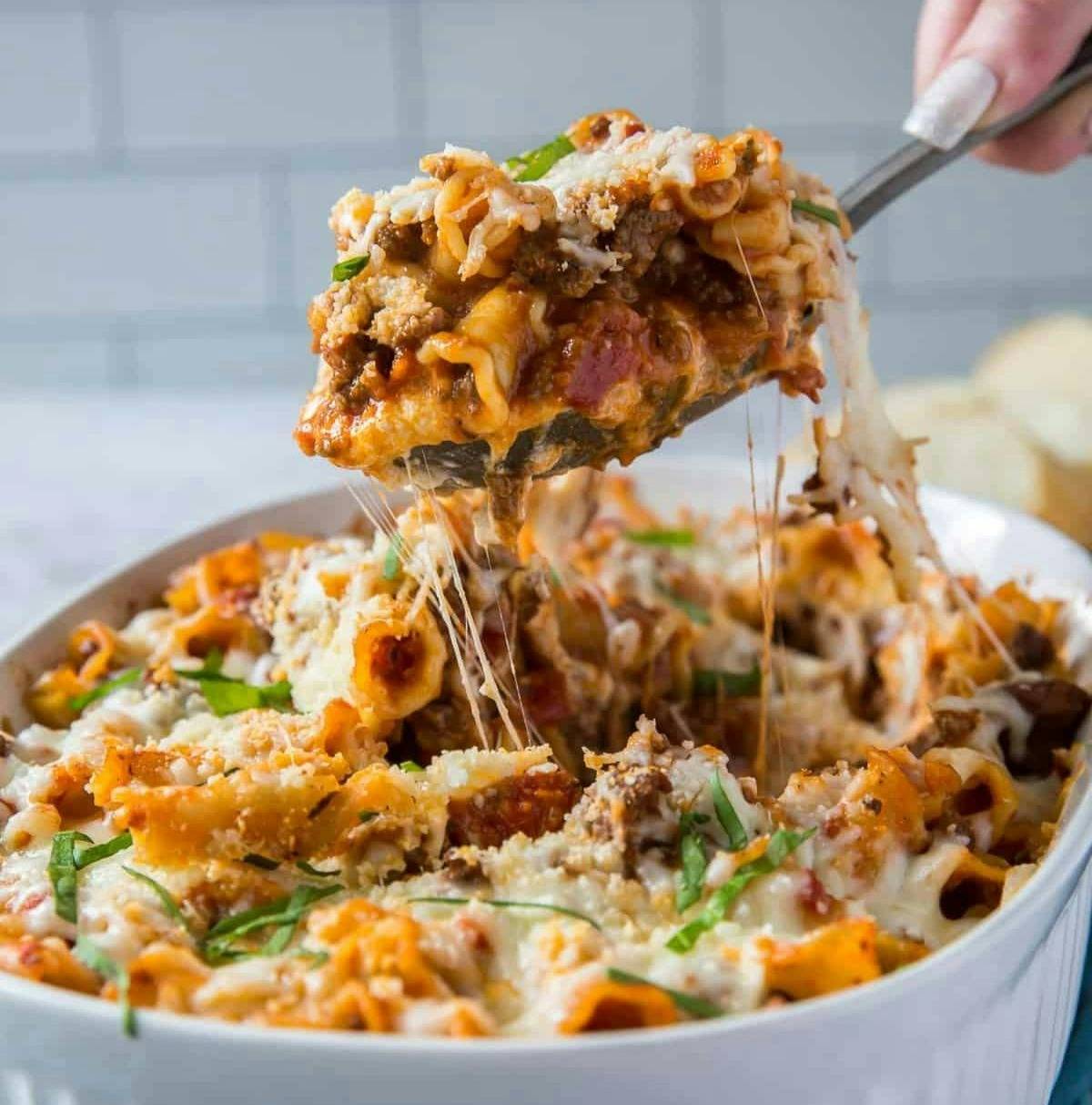 A spoon scooping lasagna from a casserole dish.