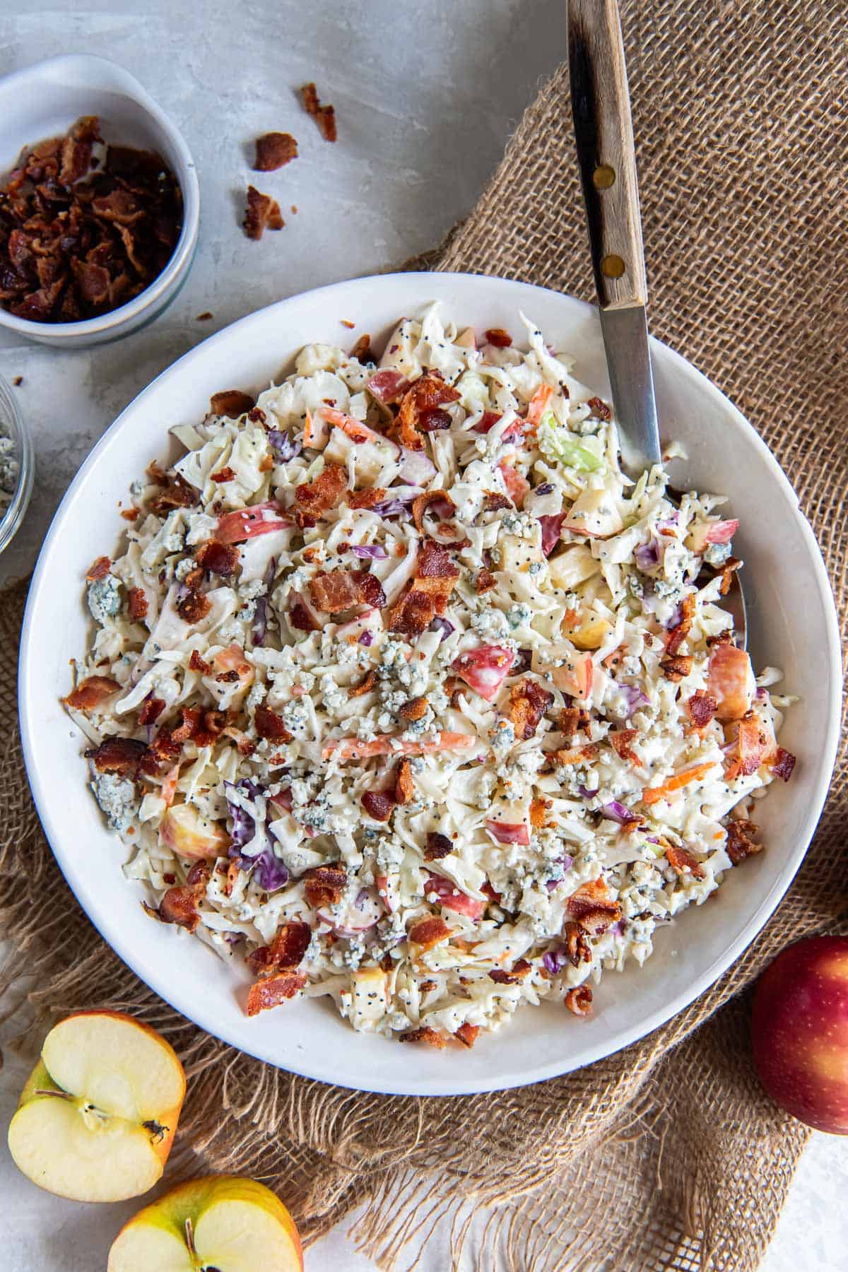 Coleslaw with apples and bacon in a large white bowl.