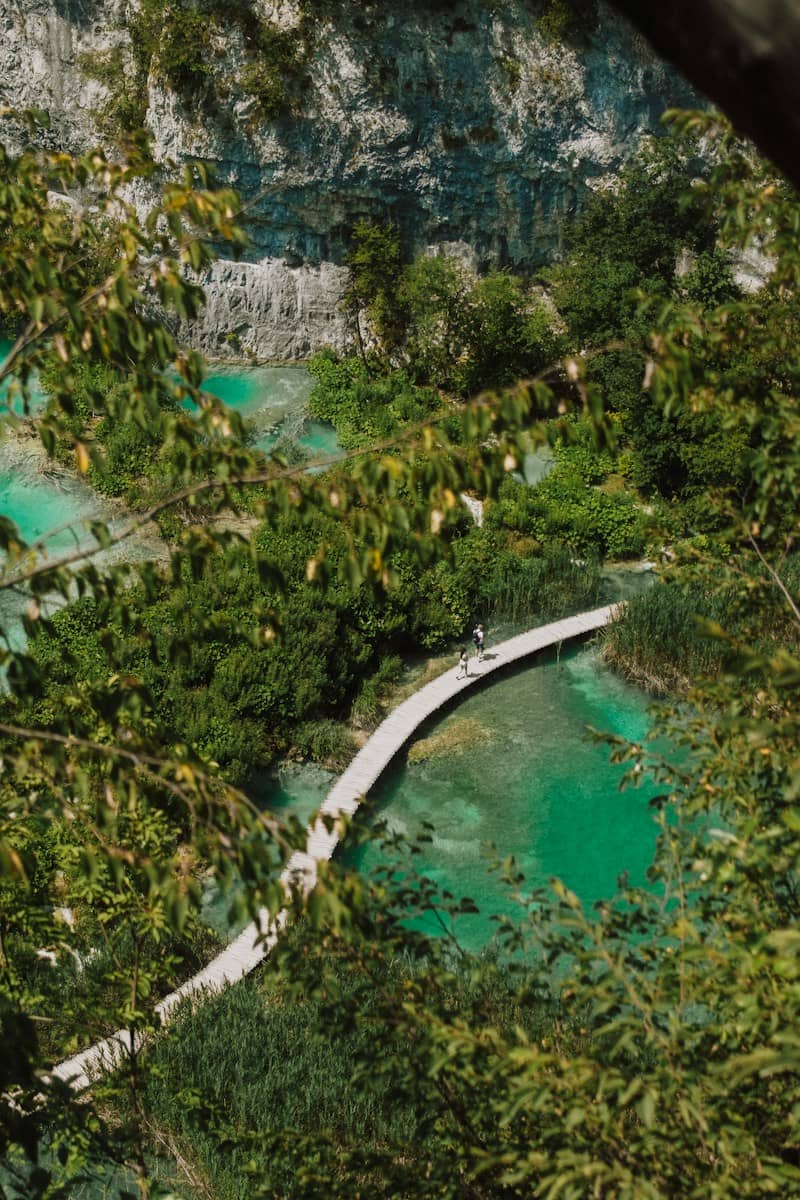 People walking on a wooden boardwalk over turquoise water in Plitvice Lakes National Park