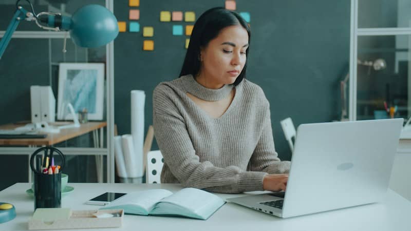 A woman in a beige sweater typing on a laptop at a desk