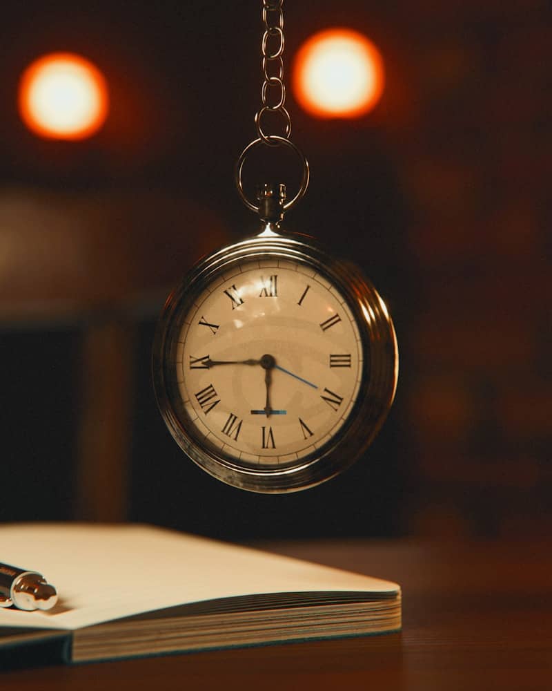 A silver pocket watch hangs above a notebook and pen.