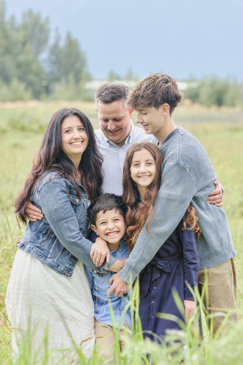A happy family of five posing in a grassy field.