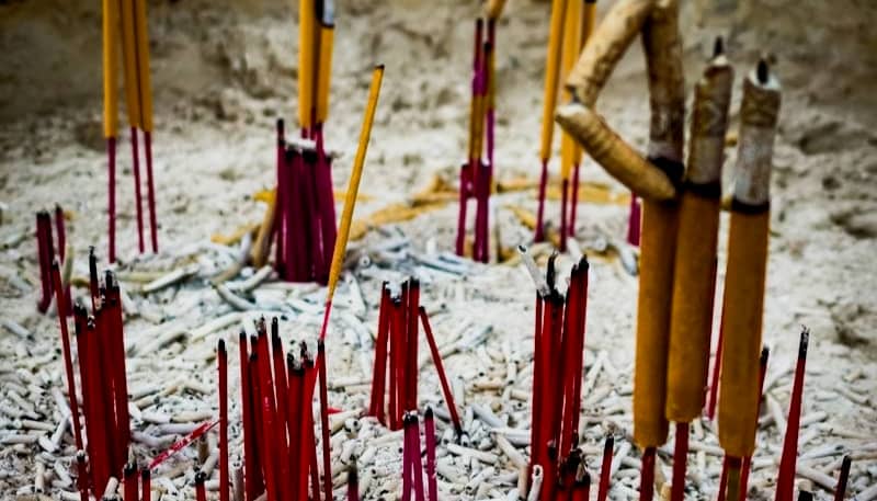 bunches of burnt and burning sticks of incense. Only the red sticks remain of most while the grond is covered in white ash. 