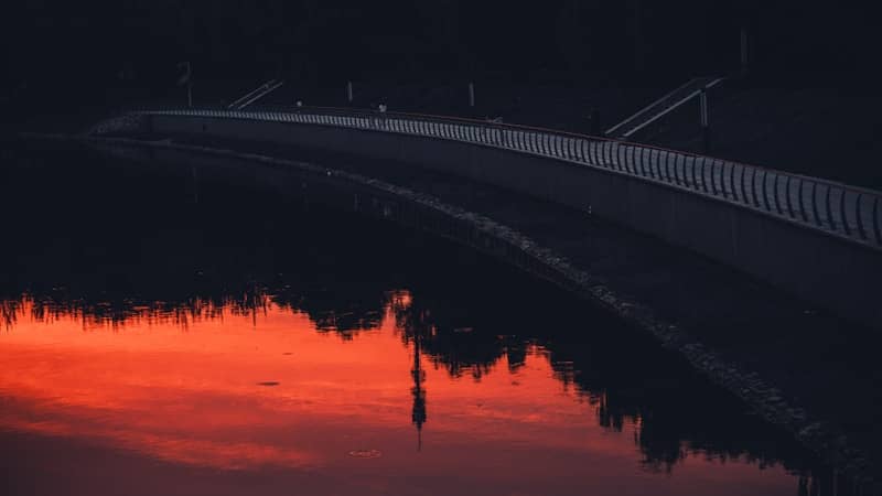 Bridge over water reflecting a vibrant sunset