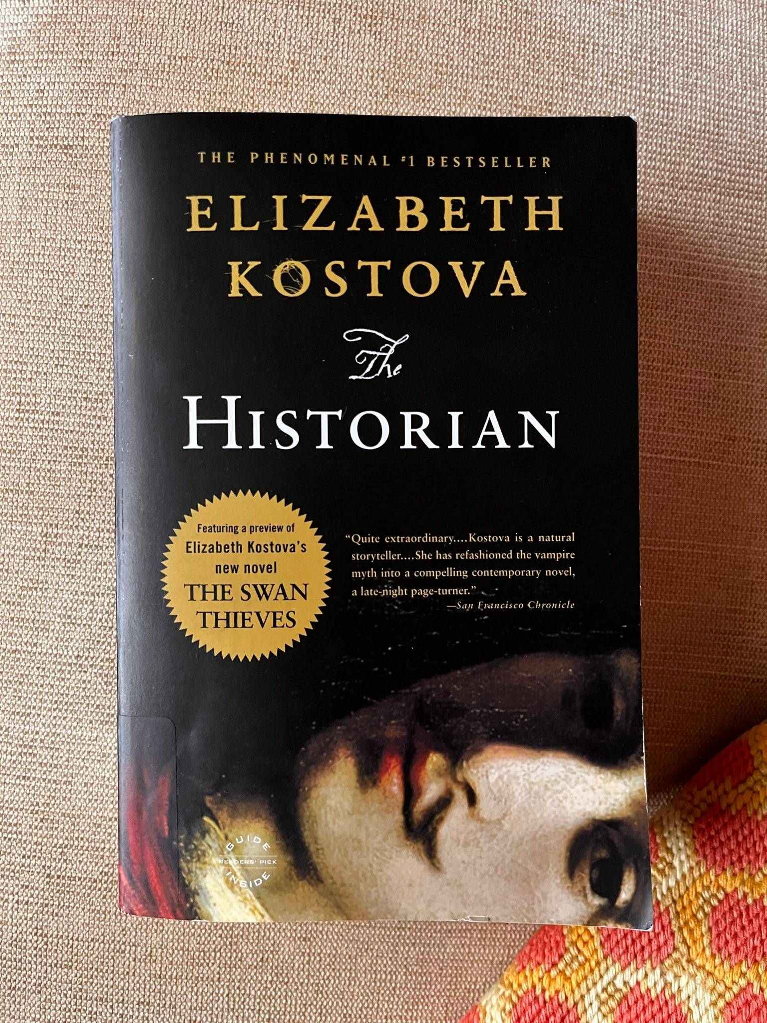 Th on a beige textured surface with an orange and yellow pillow in the lower right corner.