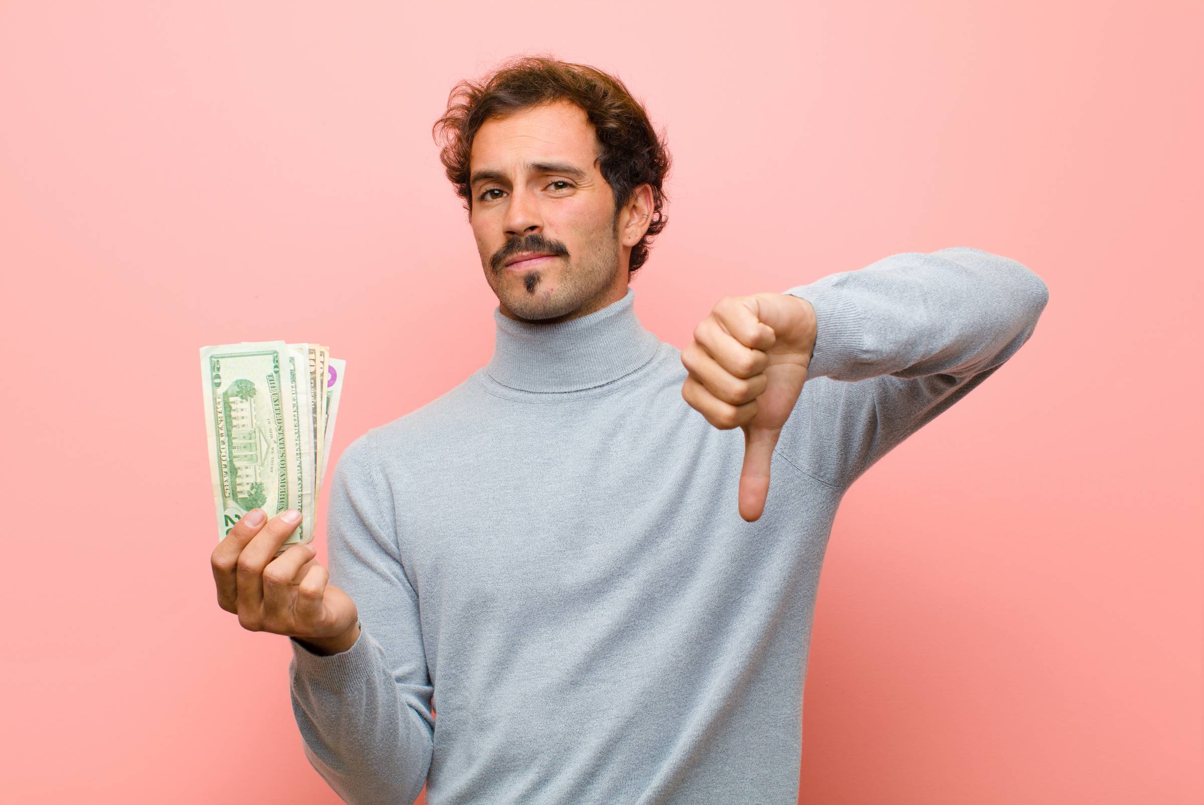 A man holding some dollar notes and doing the thumbs down sign.