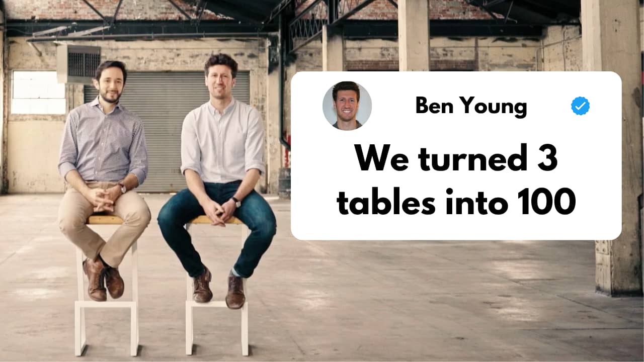 Two men sitting on minimalist white tables in an industrial space. On the right, a Twitter-style post by Ben Young with a verified checkmark says 'We turned 3 tables into 100'