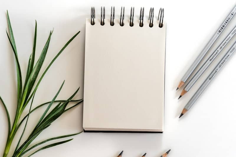 Blank notepad with pencils and green leaves