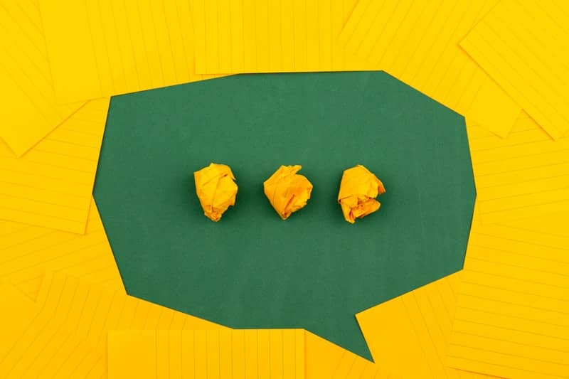 three crumpled yellow papers on green surface surrounded by yellow lined papers