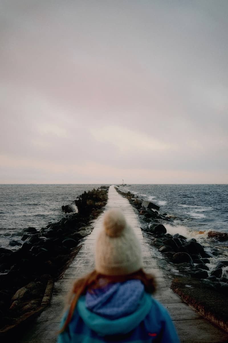 Person walks on a pier towards the ocean.