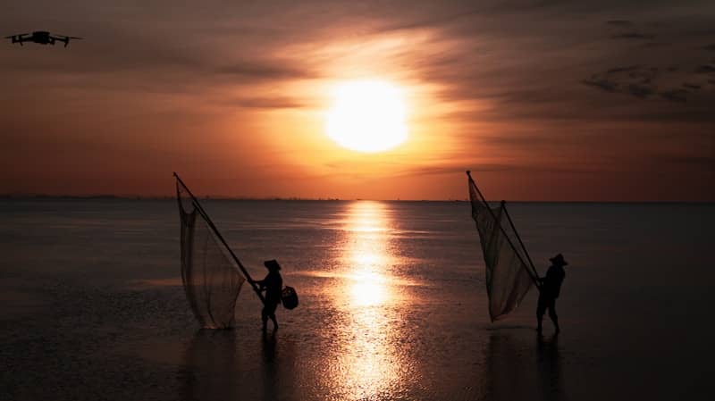 Fishermen fish at sunset with a drone overhead.