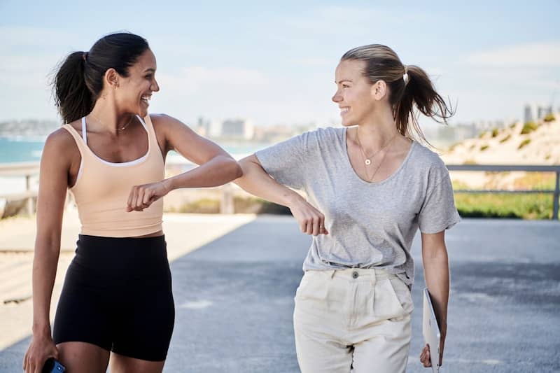 woman in gray shirt elbow bumping with woman in sports outfit