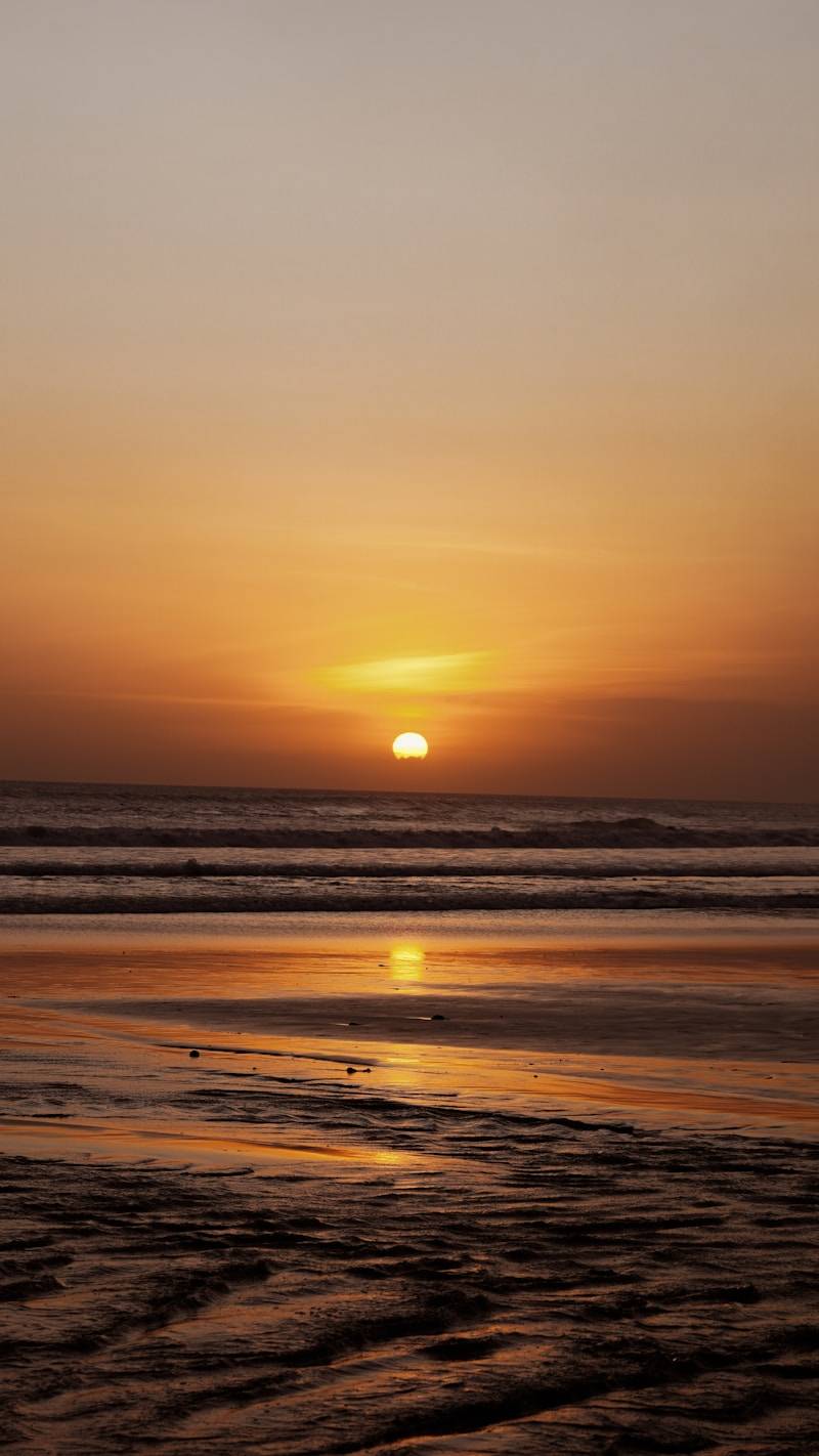 Sunset over the ocean with wet sand reflections.