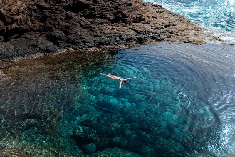 A person floats in a natural, clear tide pool.