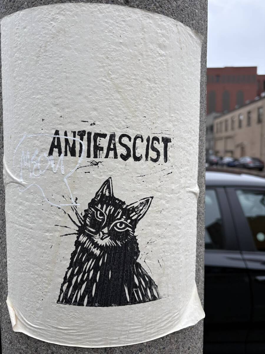 Poster pasted on a column that says "Antifascist" over a block-printed cat