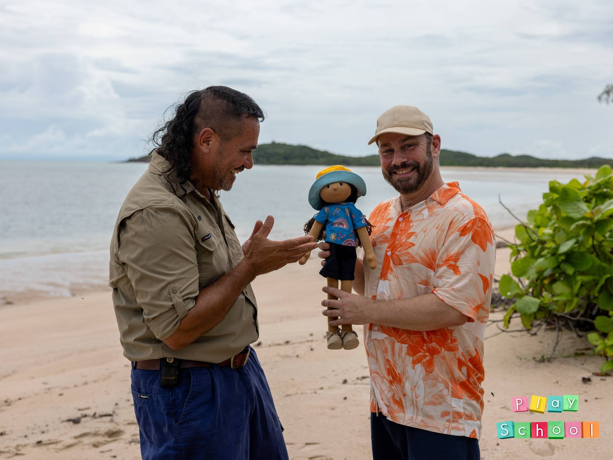 Play School presenter Teo Gebert standing with TSRA Ranger Supervisor Laurie Nona and the show's Kiya doll on Badu Island in the Torres Strait, during filming of the groundbreaking My Place, My Home: Island Life episode that highlights Torres Strait Islander culture, traditions, and environmental knowledge for young Australian audiences.