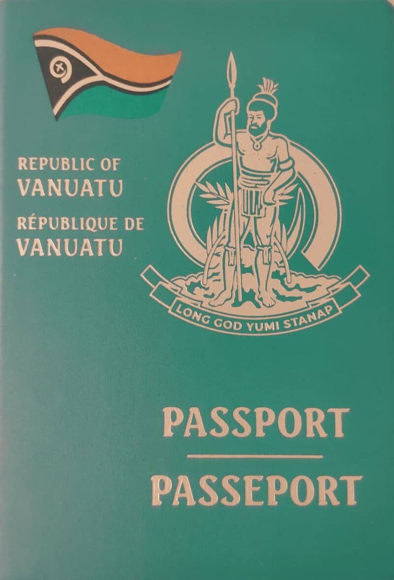 Cover of a Republic of Vanuatu passport showing the distinctive green cover with gold lettering. At the top is the Vanuatu flag with its characteristic Y-shaped design in black, red, and yellow. The central feature is Vanuatu's coat of arms depicting a traditional Melanesian warrior holding a spear, surrounded by fern leaves and boar's tusks, with the national motto 'Long God Yumi Stanap' (In God We Stand) on a banner below. The text 'REPUBLIC OF VANUATU' and 'RÉPUBLIQUE DE VANUATU' appears in both English and French above the coat of arms, with 'PASSPORT' and 'PASSEPORT' at the bottom in both languages.