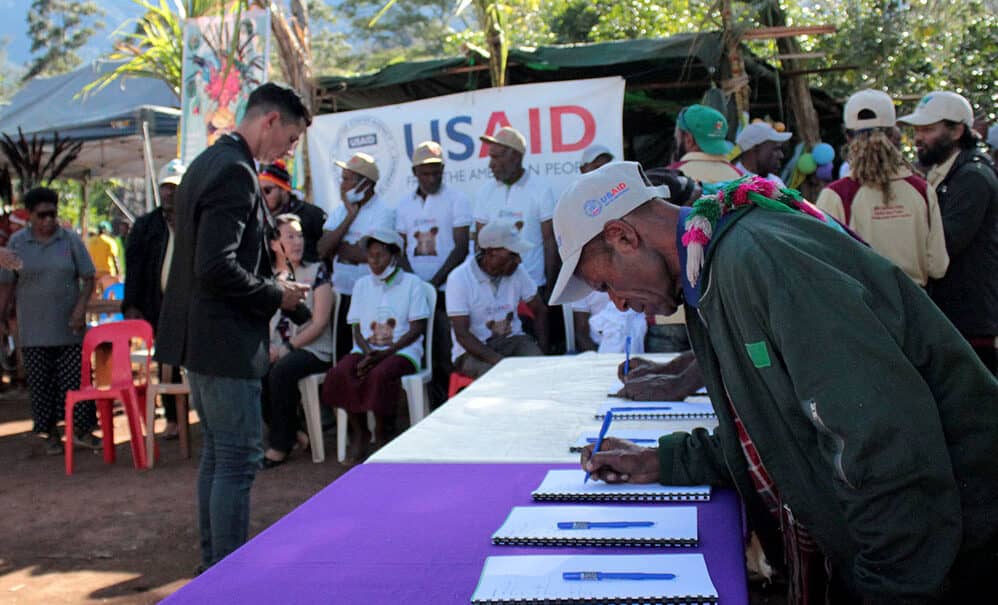 Local community members in Madang Province, Papua New Guinea, participating in a USAID-supported conservation project to protect over 40,000 hectares of forest and marine areas, with lush greenery and tropical vegetation visible in the background.